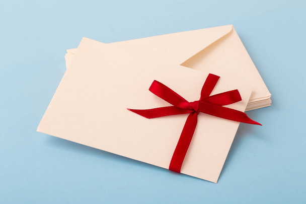 Buchstabe mit roter Schleife auf Stapel von Umschlag auf blauem Hintergrund - Foto, Bild