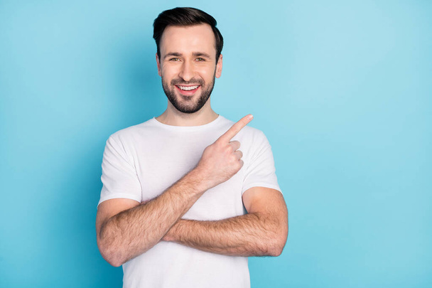 Photo of positive young man beaming smile indicate finger empty space isolated on blue color background - Fotoğraf, Görsel