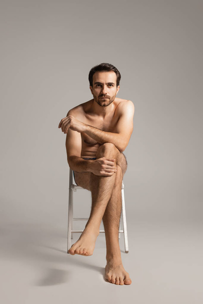 Portrait of young handsome bearded shirtless man sitting on chair isolated on white studio background. Natural beauty - 写真・画像