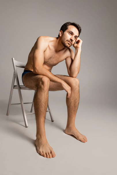 Portrait of young handsome bearded shirtless man sitting on chair isolated on white studio background. Natural beauty - Φωτογραφία, εικόνα