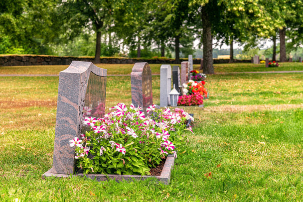 Rij grafstenen met kleurrijke bloemen op een goed verzorgde begraafplaats in Zweden - Foto, afbeelding