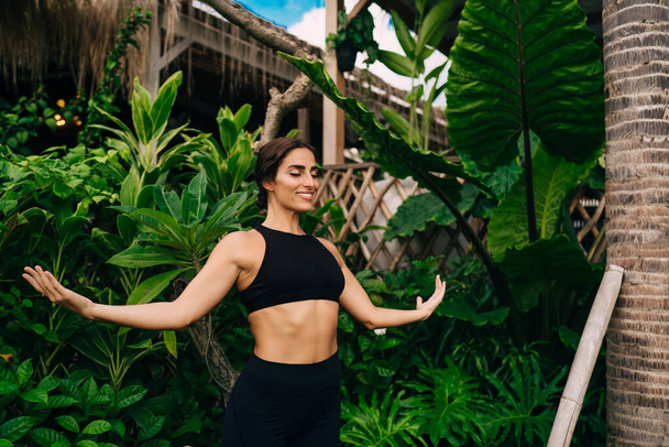 Happy female yogi practicing hatha during leisure time for mental harmony keeping healthy lifestyle, cheerful Caucasian woman in black top feeling freedom and pleasure while recreating outdoors - Foto, immagini