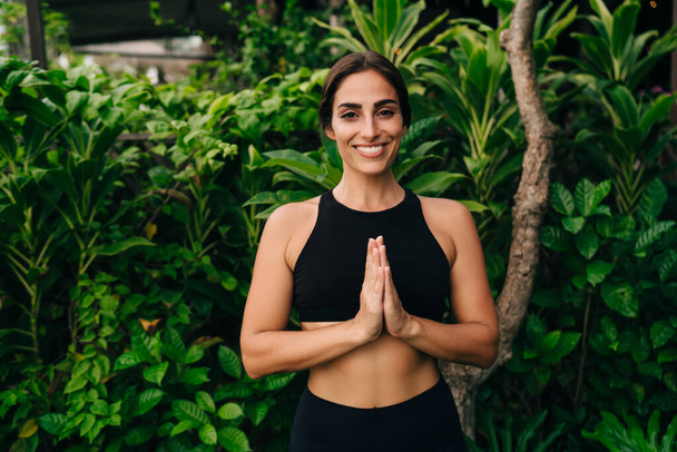 Half length portrait of cheerful Caucasian female yogi in namaste pose smiling at camera during relaxing recreation, happy woman enjoying healthy lifestyle keeping mental vitality with yoga - Фото, изображение