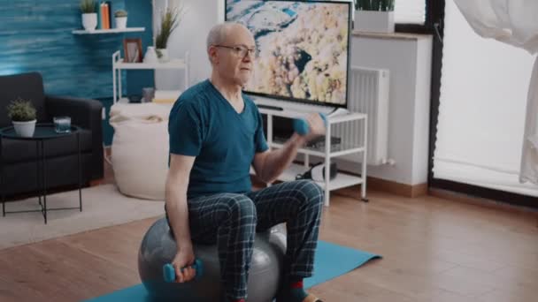 Senior mężczyzna podnoszenie hantli i siedzi na fitness toning ball - Materiał filmowy, wideo