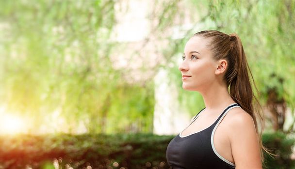 Beautiful smiling young woman with ponytail, breathing fresh air in the park. Woman enjoying yoga, relaxing, got freedom. Copy space background. Side view portrait. Sunlight. Gym, lifestyle concept.  - Foto, Bild