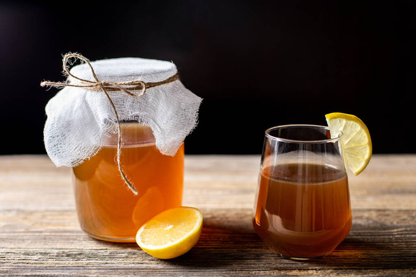 Raw fermented homemade alcoholic or non alcogolic kombucha superfood. Ice tea with healthy natural probiotic in glass with lemon slice on wooden background - Φωτογραφία, εικόνα