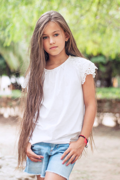 Beautiful school girl with long hair in the park.  Prety Girl with a model appearance and with fashionable poses. Child of 8 years. - Foto, Bild