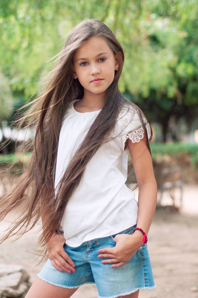 Gyönyörű iskolás lány hosszú hajjal a parkban. Prety Girl modell megjelenéssel és divatos pózokkal. 8 éves gyermek. - Fotó, kép