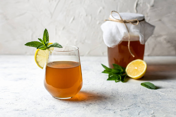 Сирий ферментований домашній алкогольний або неалкогольний комбуча суперпродукт. льодовий чай зі здоровим природним пробіотиком у склянці з лимонним шматочком та м'ятою на білому тлі
 - Фото, зображення