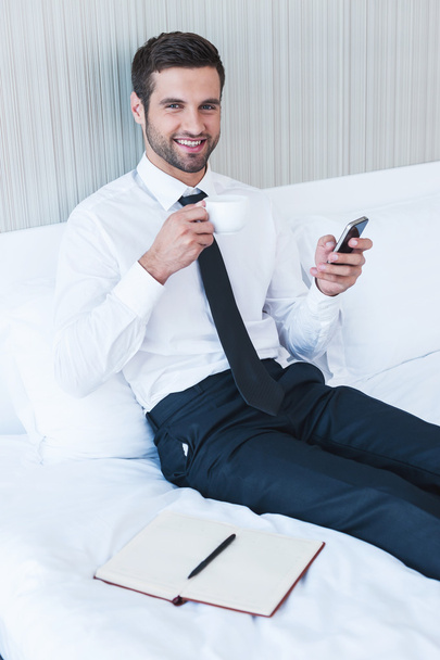 Man in shirt and tie drinking coffee and holding mobile phone - Fotoğraf, Görsel