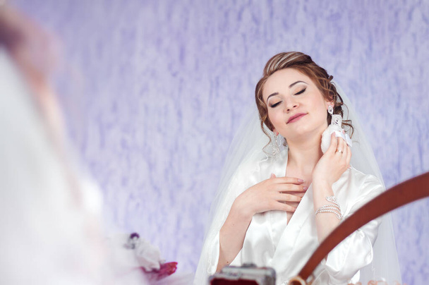 Morning of the bride. The bride is having a look at the mirror. Portrait of a beautiful and young bride. Powder make up.   Bride applying wedding make-up - Foto, Bild