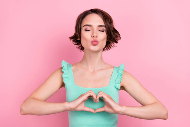 Photo of romantic bob hairdo young lady blow kiss hands heart wear teal top isolated on pink color background - Foto, Imagen