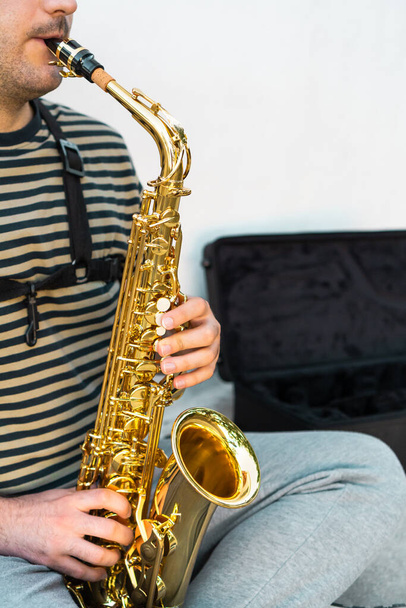 Musician sitting and playing saxophone in front of a white wall. - Φωτογραφία, εικόνα