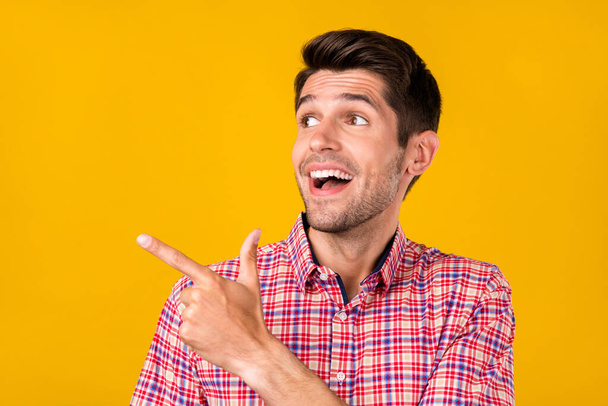 Portrait of attractive amazed cheerful guy demonstrating copy empty space ad isolated over bright yellow color background - Foto, Imagem