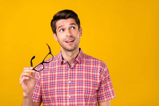 Portrait of attractive cheerful guy holding in hand specs creating solution copy space isolated over vibrant yellow color background. - Foto, Imagem