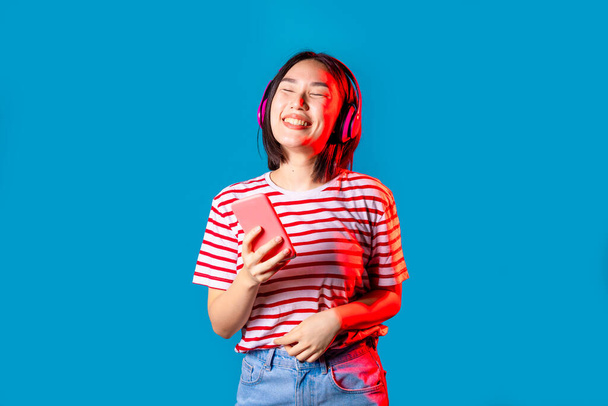 Joven mujer asiática en el interior aislado fondo bailando escuchando música auriculares inalámbricos celebración de smartphone - Foto, Imagen