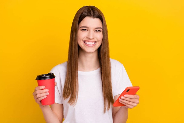 Photo of young happy positive woman smile hold phone takeout coffee smile isolated on shine yellow color background - Foto, afbeelding