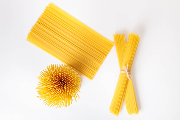 A vertical bunch and a bunch of raw spaghetti tied with string. Bundle on a white background. View from above. Italian food concept. - Fotografie, Obrázek