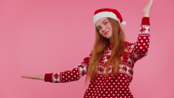 Woman wears red New Year sweater deer showing thumbs up and pointing at on blank advertisement space - Footage, Video