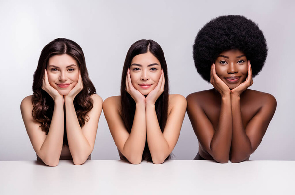 Photo de trois jeunes femmes heureux sourire positif mains toucher joues hydratation cosmétologie isolé gris fond de couleur - Photo, image
