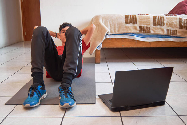 Hombre latino joven haciendo ejercicio, crujir, usando el ordenador portátil en casa. - Foto, imagen