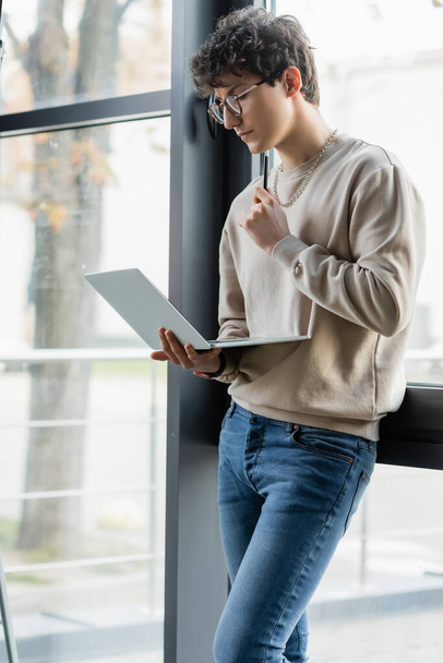 Mladý podnikatel drží pero a notebook v blízkosti okna v kanceláři  - Fotografie, Obrázek