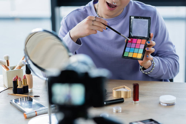 Cropped view of transgender person holding eye shadows near cosmetics and digital camera  - Photo, Image
