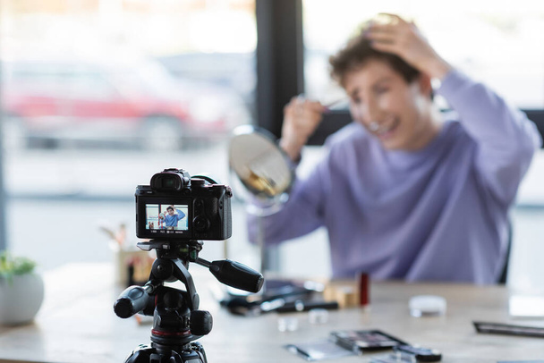 Digital camera near blurred transgender person with cosmetic brush and decorative cosmetics  - Valokuva, kuva