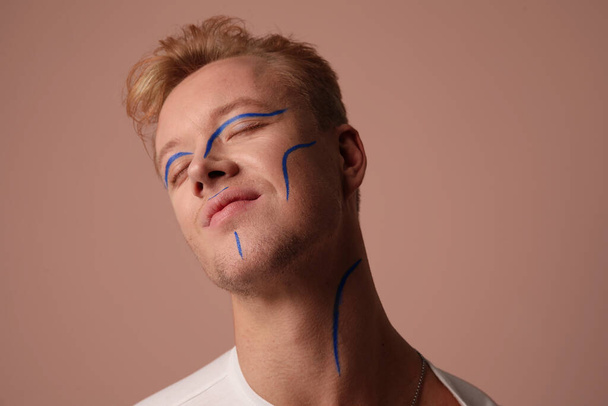 Portrait of male model wears funky make-up in blue. Posing in the studio. - Fotó, kép
