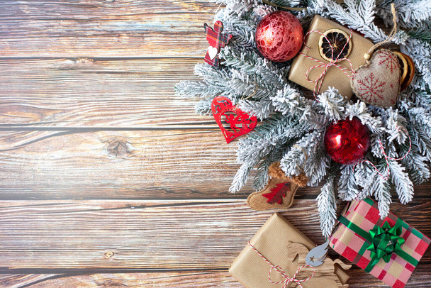 Ramos de abeto na neve decorados com decorações de Natal e caixas de presente embrulhadas estão em um fundo de madeira. Espaço livre para texto. - Foto, Imagem