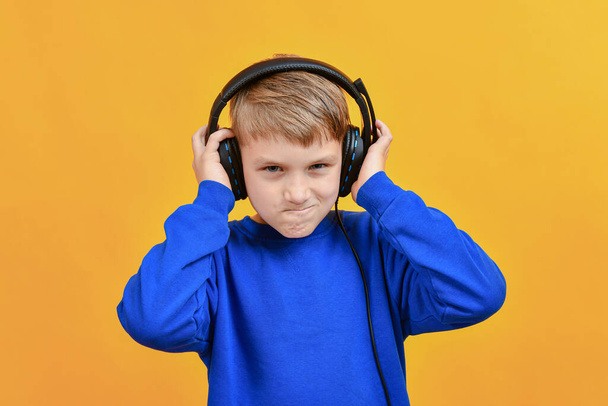 Um menino com fones de ouvido se alegra com a música e olha para frente. - Foto, Imagem