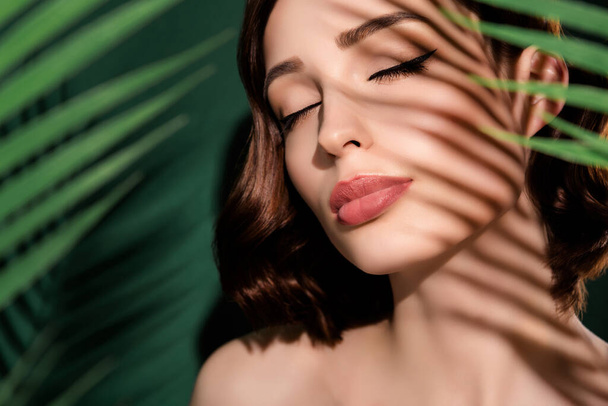 Portrait of young happy dreamy female with closed eyes spa treatment procedure isolated on green floral background - Foto, immagini