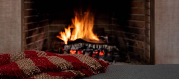  Χαλάρωση κοντά στη φωτιά, Χριστούγεννα διακοπές ζεστό εσωτερικό σπίτι. Κουβέρτα στον καναπέ, τζάκι καύση ξύλου κορμούς φόντο - Φωτογραφία, εικόνα