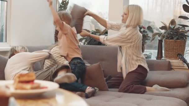 Široký záběr kavkazského chlapečka a tří dospívajících dívek, jak se perou na gauči doma v obývacím pokoji a baví se ve dne - Záběry, video