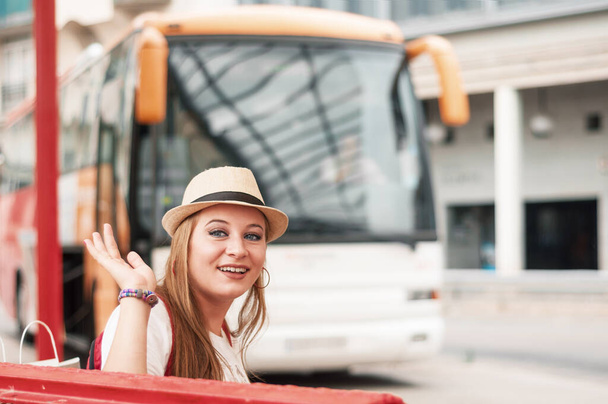 Traveler girl waves her hand at the bus station, waiting for her boy friend. New acquaintances, meetings and travel. - Photo, Image