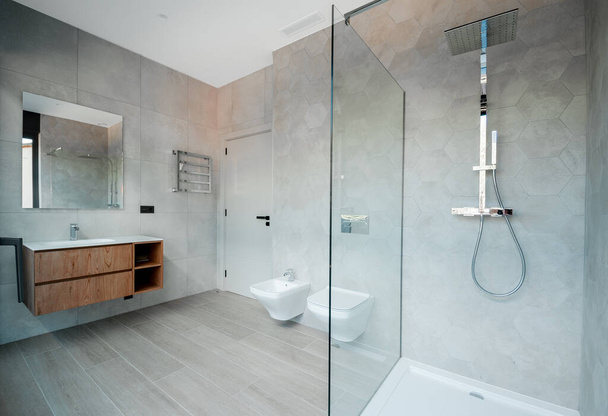 Сучасна ванна кімната зі скляною ванною і розкішним умивальником. Стіни і підлога покриті сучасною плиткою
.  - Фото, зображення