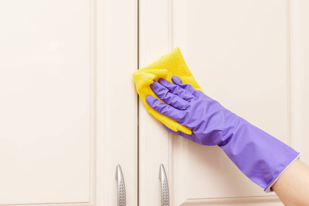 female hand in a purple rubber glove wipes the beige kitchen cabinet door. Yellow rag in hand - Foto, Imagem