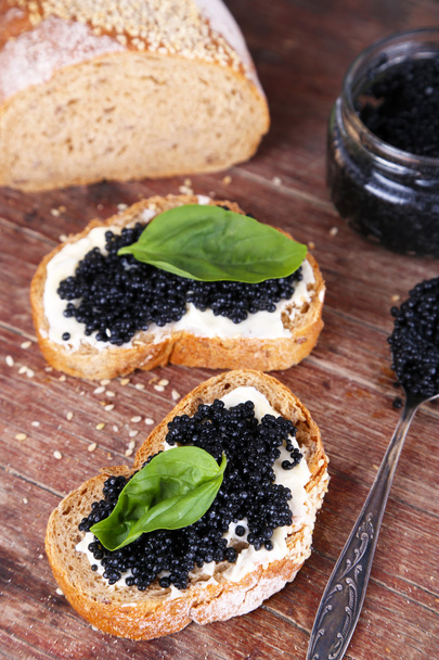 Slices of bread with butter and black caviar on wooden background - Фото, изображение