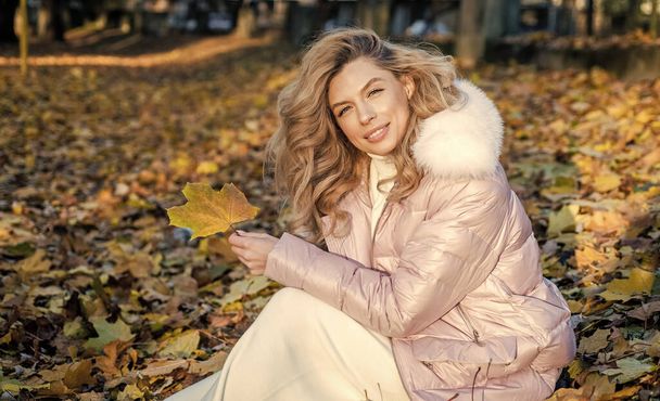 Enjoying autumn day. fallen leaves. nature beauty. beautiful blonde woman in puffer coat. autumn fashion and beauty. pretty girl has long curly blond hair. lady in fall padded jacket in forest - Фото, изображение