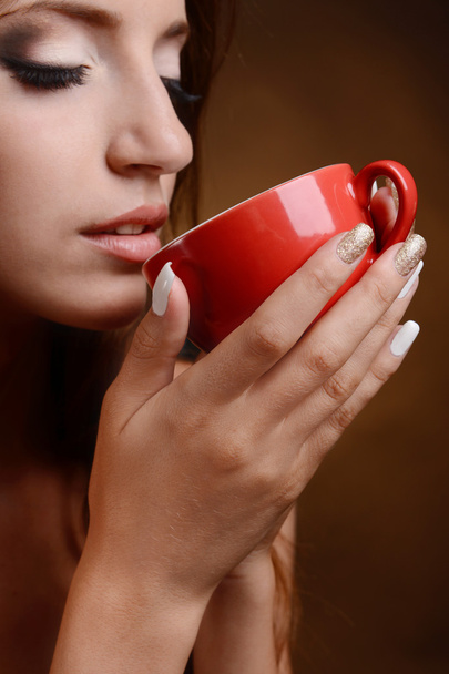 Beautiful young girl with cup of coffee on brown background - Foto, afbeelding