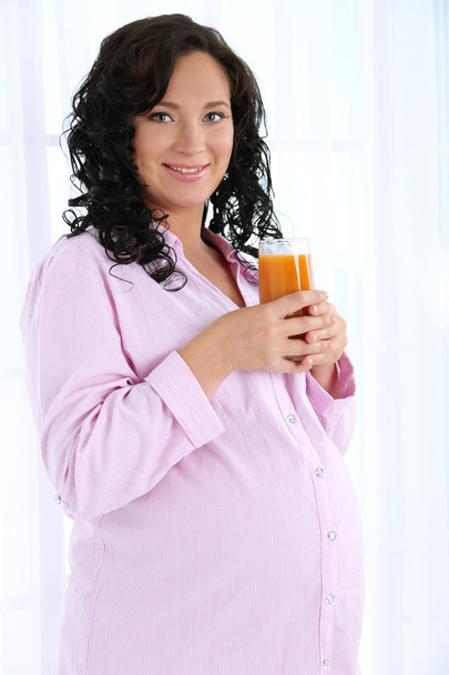 Young pregnant woman holding glass of juice on light background - Fotoğraf, Görsel