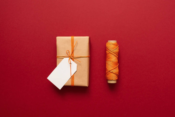 Kraft lahjapakkaus oranssi lanka ja etiketit kirjoituksia punaisella pohjalla. Lahjojen pakkaaminen ja valmistelu juhlaa varten. Joulun uusi vuosi tausta - Valokuva, kuva