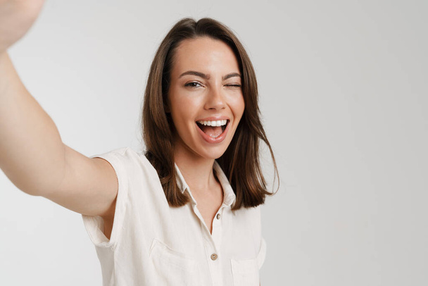 Young european woman winking while taking selfie photo isolated over white background - Foto, Bild