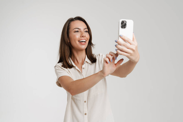 Young european woman taking selfie photo on mobile phone isolated over white background - Photo, Image