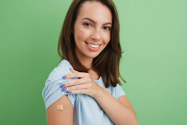 Young brunette woman laughing while showing her bandage isolated over green background - Fotó, kép