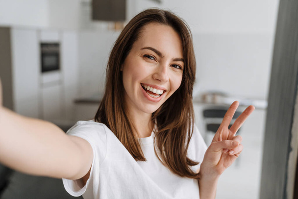 Young white woman smiling and gesturing while taking selfie photo, indoors - Foto, immagini