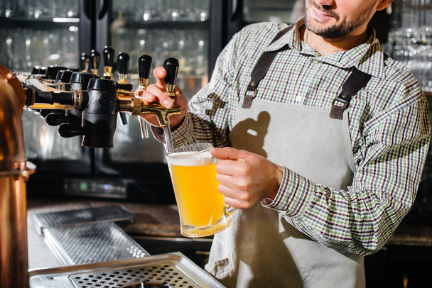 Close-up of a bearded bartender filling a mug of lager beer. The bar counter in the pub. - Photo, image