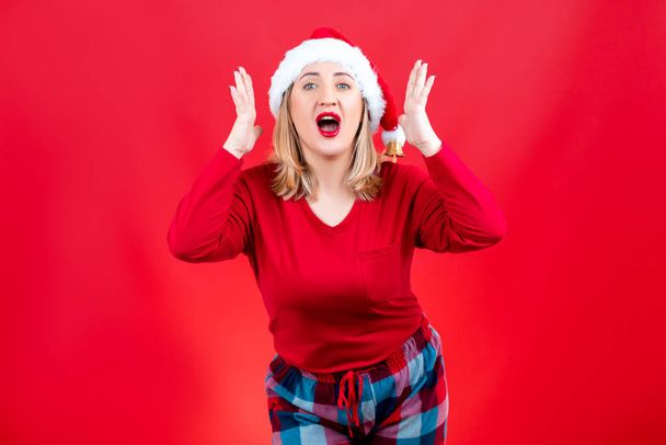 uma loira em um fundo vermelho ou um chapéu de Papai Noel agarra a cabeça e mostra emoção - Foto, Imagem