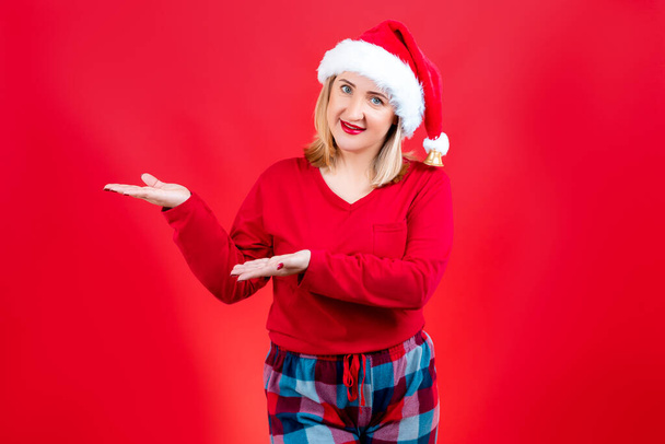 loira em um fundo vermelho de Natal e pijama mostra o lado com as palmas das mãos - Foto, Imagem