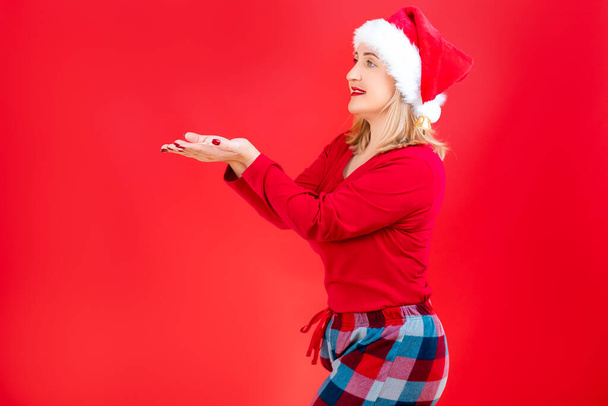 blonde kerstman hoed staat zijwaarts en strekt haar handpalmen naar voren - Foto, afbeelding